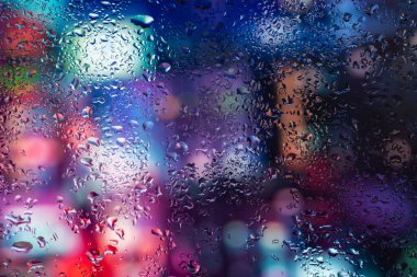 Pencere camındaki yağmur damlaları ve buğulanma gece şehrinin arka planına karşı.