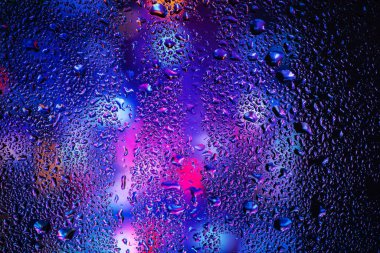 Pencere camındaki yağmur damlaları ve yoğunlaşma neon ışığının arka planına karşı.