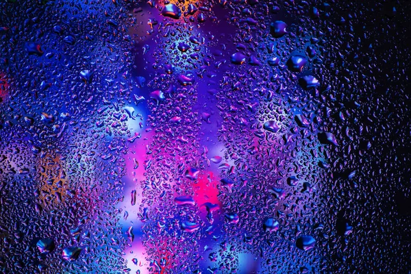 Pencere camındaki yağmur damlaları ve yoğunlaşma neon ışığının arka planına karşı.