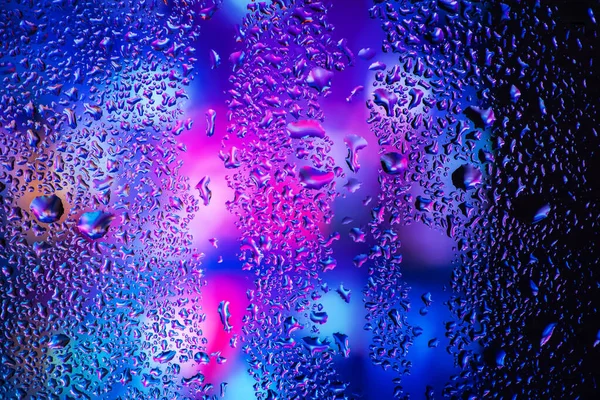 Pencere camındaki yağmur damlaları ve yoğunlaşma neon ışığının arka planına karşı.