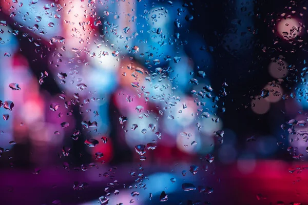 Pencere camındaki yağmur damlaları ve buğulanma gece şehrinin arka planına karşı.