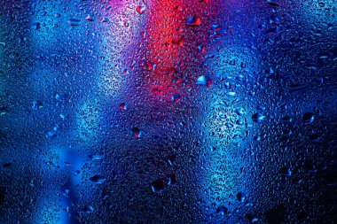 Pencere camındaki yağmur damlaları ve yoğunlaşma neon ışığının arka planına karşı.