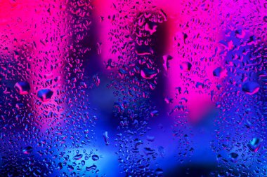 Pencere camındaki yağmur damlaları ve yoğunlaşma neon ışığının arka planına karşı.