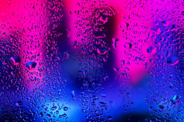 Pencere camındaki yağmur damlaları ve yoğunlaşma neon ışığının arka planına karşı.