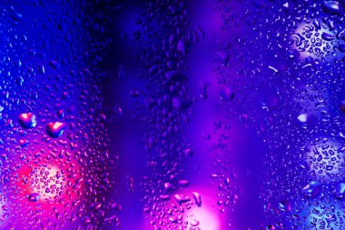 Pencere camındaki yağmur damlaları ve yoğunlaşma neon ışığının arka planına karşı.