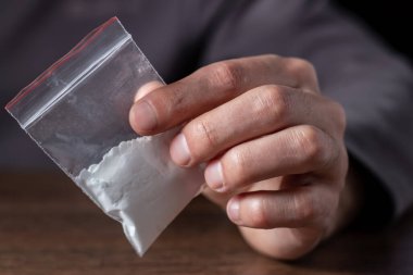 Konsept uyuşturucu bağımlılığı. Bir erkek elinde plastik paket ya da torba kokain ya da başka bir uyuşturucu, uyuşturucu bağımlılığı ve tehlike bağımlılığı kavramı taşır.