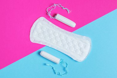 Kadın pedleri ve tamponları - hijyenik pedlerin yanında pembe ve mavi arka planda izole edilmiş bir tampon bulunur. Kadın hijyeni ve adet dönemi konsepti