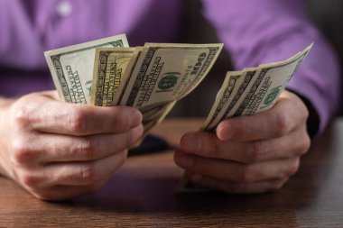 Bir adam 100 dolarlık banknotları elinde tutuyor.