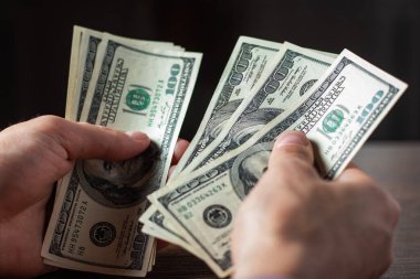 Bir adam 100 dolarlık banknotları elinde tutuyor.