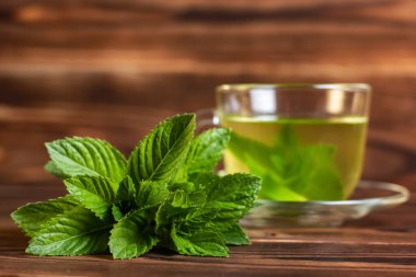 Ahşap zemin üzerinde taze nane yaprakları ve naneli bir fincan çay..
