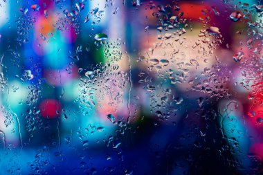 Pencere camındaki yağmur damlaları ve buğulanma gece şehrinin arka planına karşı.