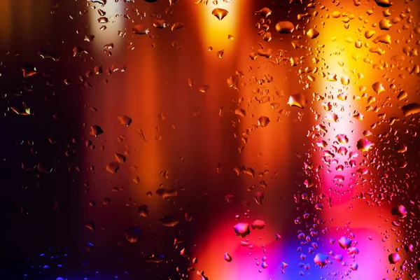 Drops of condensate on the sweaty glass. Cold foggy glass on background night lights.