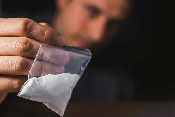 Konsept uyuşturucu bağımlılığı. Bir erkek elinde plastik paket ya da torba kokain ya da başka bir uyuşturucu, uyuşturucu bağımlılığı ve tehlike bağımlılığı kavramı taşır.