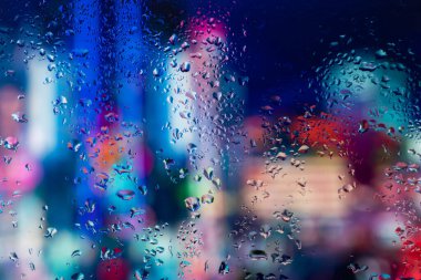 Pencere camındaki yağmur damlaları ve buğulanma gece şehrinin arka planına karşı.