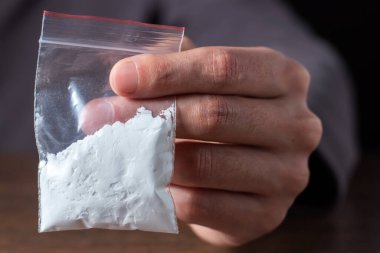 Konsept uyuşturucu bağımlılığı. Bir erkek elinde plastik paket ya da torba kokain ya da başka bir uyuşturucu, uyuşturucu bağımlılığı ve tehlike bağımlılığı kavramı taşır.