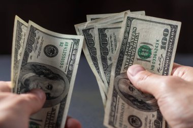 Bir adam 100 dolarlık banknotları elinde tutuyor.