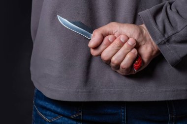 Criminal with knife weapon hidden behind his back. clipart