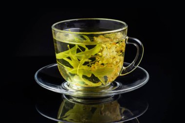 Siyah arka planda bir fincan yeşil çay ve ıhlamur..