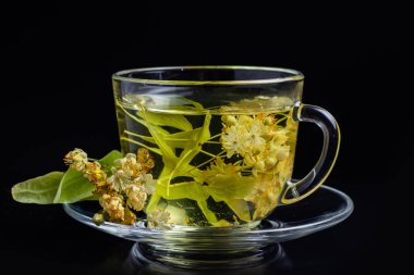 Siyah arka planda ıhlamur çiçekleri olan bir fincan bitki çayı..