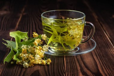 Tahta arka planda ıhlamur çiçekleri olan bir fincan bitki çayı..