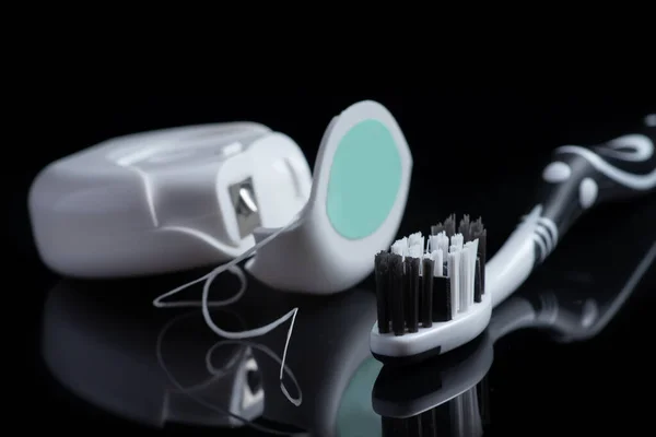 Close up of toothbrush and dental floss on black.