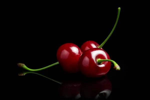 Red cherry berries on a black background with mirror. Three cherries.