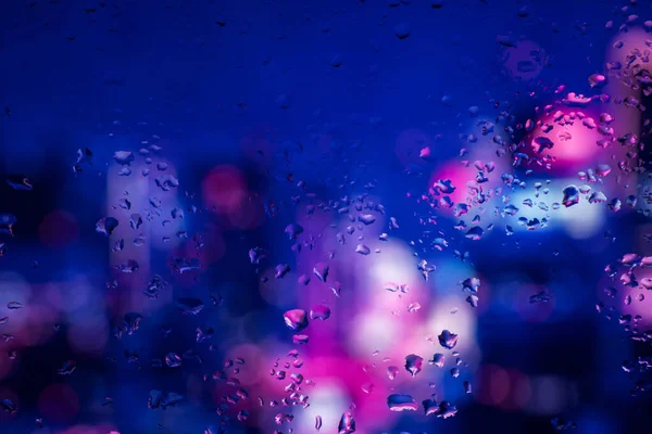 Pencere camındaki yağmur damlaları ve yoğunlaşma neon ışığının arka planına karşı.