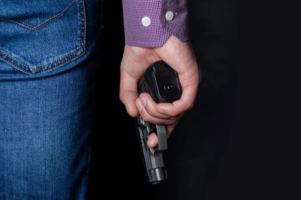 A man holding a gun in his hand behind his back, close-up view. Concepts: crime, attempted murder, a gunshot wound, the killer, robbery