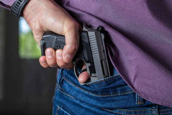 A man holding a gun in his hand behind his back, close-up view. Concepts: crime, attempted murder, a gunshot wound, the killer, robbery