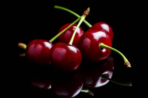 Red cherry berries on a black background with mirror. Three cherries.