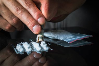Kokain barutu kullanmak için banknot tutan bir adam. Uyuşturucu bağımlılığı konsepti. Siyah arka planda bir sıra kokain. Bağımlılık kavramı. Mephedrone, amfetamin, eroin. Ciddi bağımlılık