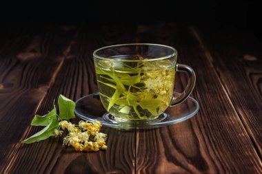 Tahta arka planda ıhlamur çiçekleri olan bir fincan bitki çayı..