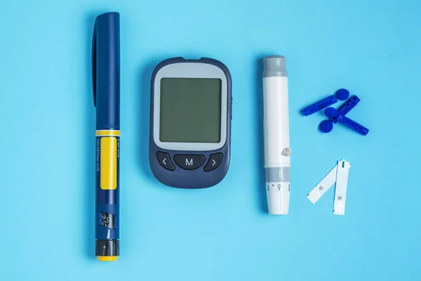 Measuring blood sugar. Glucometer, insulin pen, lancet and test strip on a blue background