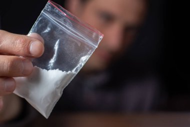 Konsept uyuşturucu bağımlılığı. Bir erkek elinde plastik paket ya da torba kokain ya da başka bir uyuşturucu, uyuşturucu bağımlılığı ve tehlike bağımlılığı kavramı taşır.