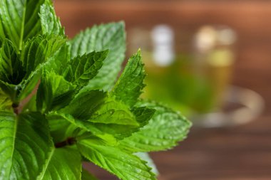 Ahşap zemin üzerinde taze nane yaprakları ve naneli bir fincan çay..
