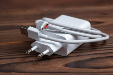Tahta arka planda USB kablosu olan beyaz şarj aleti.
