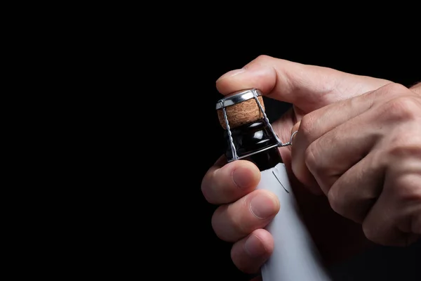 Man's hand opens a bottle of champagne. The man unscrews the champagne muselet. Champagne bottle on a black background