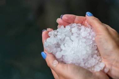 Holding freezing granulated hail ice crystals, grains in hands after strong hailstorm in autumn, fall. First snow in early winter. Cold weather