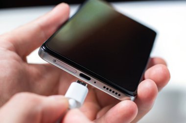 Bir akıllı telefonu USB kablosu ve güç kaynağıyla şarj etmek. USB kablosuyla asılı siyah bir akıllı telefon. Kablolu şarj
