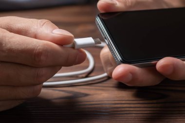 Bir akıllı telefonu USB kablosu ve güç kaynağıyla şarj etmek. USB kablosuyla asılı siyah bir akıllı telefon. Kablolu şarj