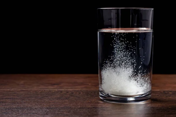 Effervescent tablet in a glass of water close-up on a black background. The concept of health