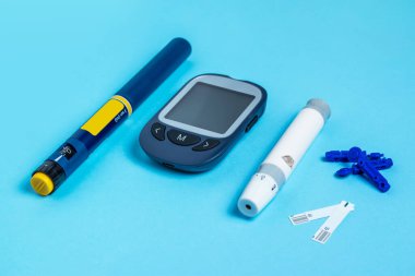 Measuring blood sugar. Glucometer, insulin pen, lancet and test strip on a blue background