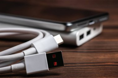 Taşınabilir alüminyum güç bankası, USB kablosu ve ahşap arka planda akıllı telefonu var..