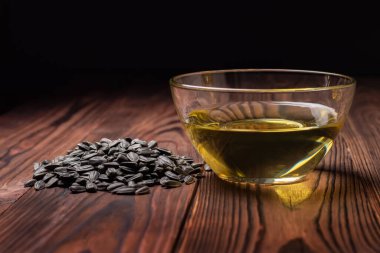 Cam kasede ayçiçeği yağı ve ahşap masa üzerinde tohum yığını..