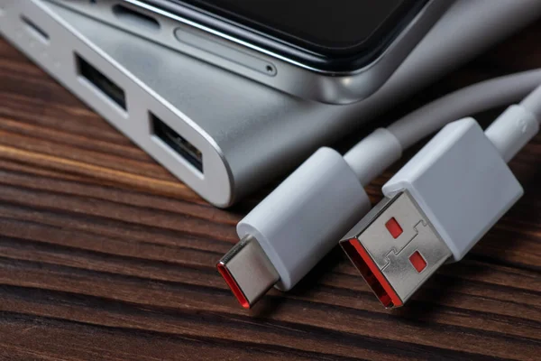 Taşınabilir alüminyum güç bankası, USB kablosu ve ahşap arka planda akıllı telefonu var..