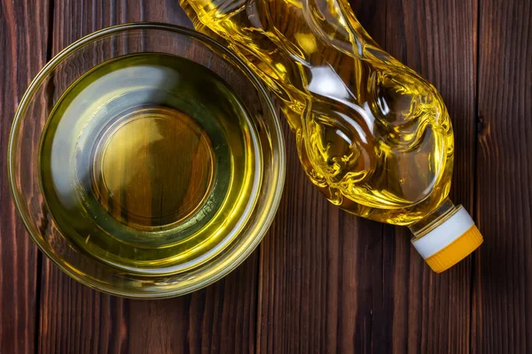 Sunflower oil in bottles with glass bowl on wooden background. Top view.