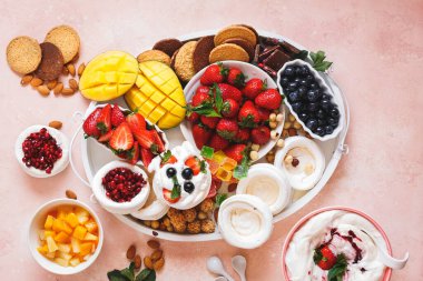 Pavlova otlatma tabağı içinde pavlova yuvaları, taze meyveler, zencefilli kurabiyeler, malzemeler, çikolata ve krema. Üst görünüm, boş boşluk