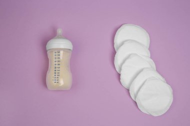 Meme sütü şişesi, eflatun arka planda göğüs uçları. Göğüs yastıkları. Giysilerdeki lekeler. Hiperlaktasyon. Süt rezervleri. Emzirme. Süt.