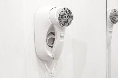 A white hairdryer is hanging on the wall in the bathroom. Photo in the interior.