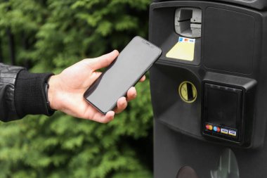 man hand pays for parking space at the parking meter by telephone